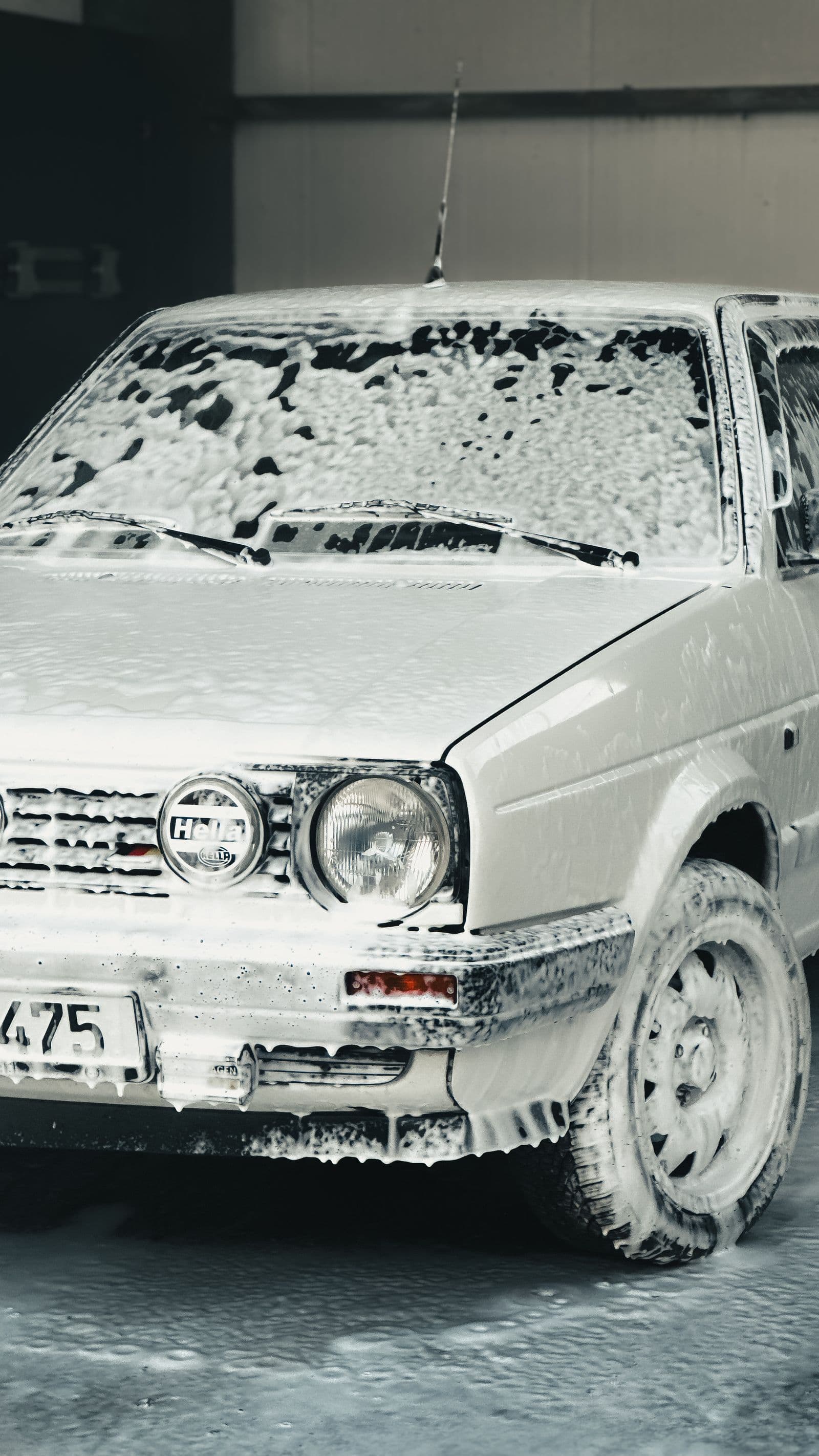 Car covered in wash foam being hand-detailed